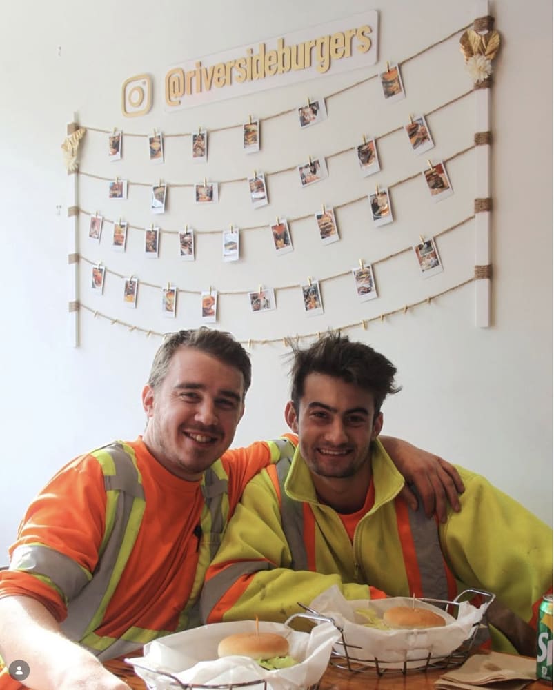 Two regulars with their burgers in front of the photo wall
