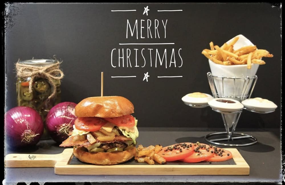 Burger and fries plated on a board with a Merry Christmas chalkboard behind